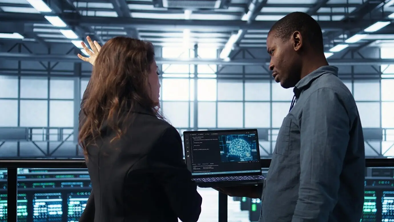 Специалист по ИТ в серверной пишет код на ноутбуке с использованием искусственного интеллекта.